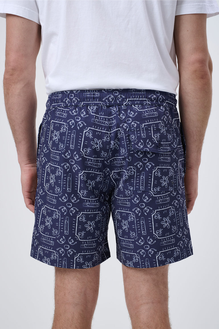 Rear view of navy swim shorts with white abstract floral and geometric print worn with a white t-shirt