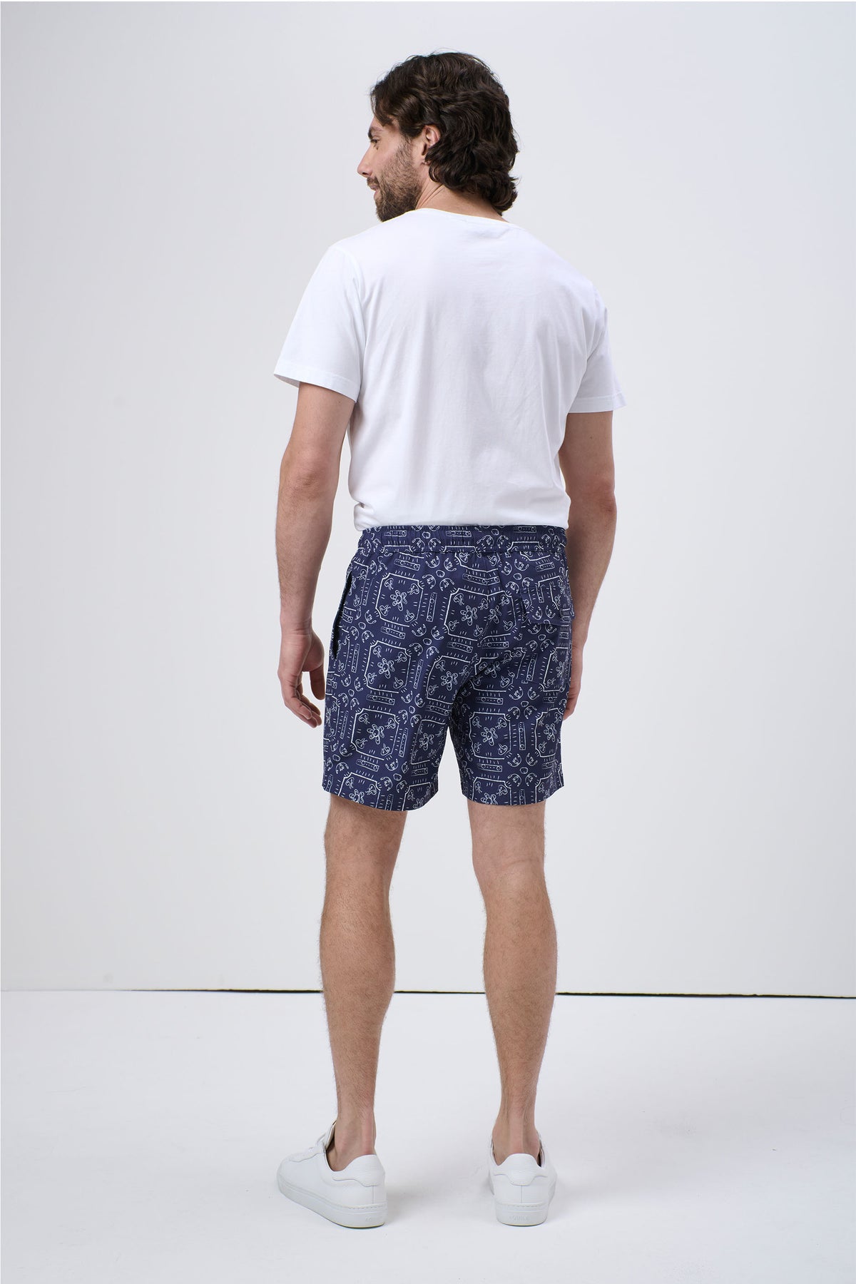 Man wearing navy blue patterned swim shorts paired with a plain white t-shirt and white sneakers, back view