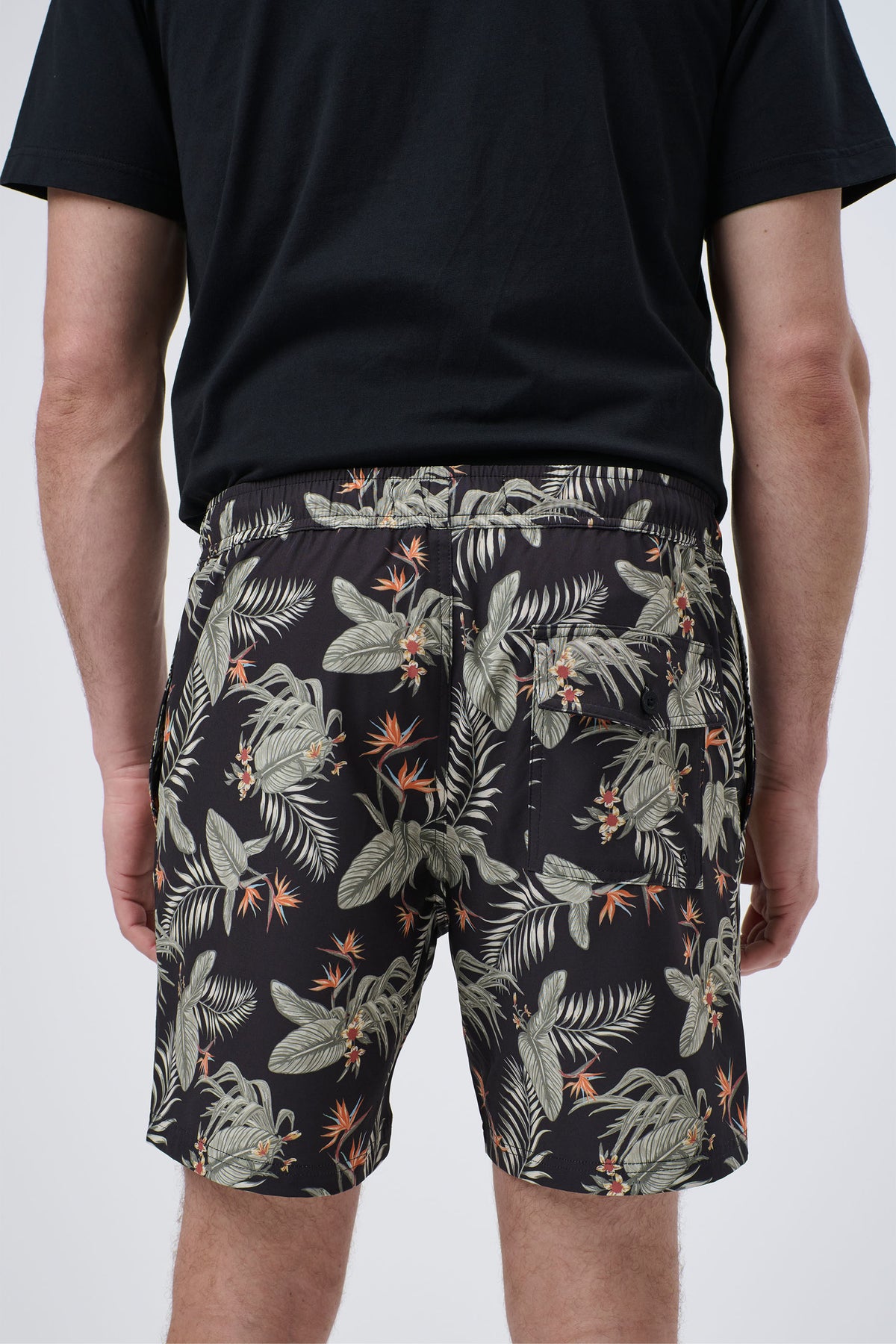 Rear view of men's swim shorts with an elastic waist and tropical leaf and flower print on black fabric