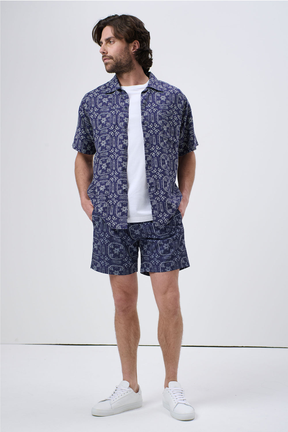 Man wearing patterned navy blue short-sleeve Cuban shirt and matching shorts with white sneakers, casual look