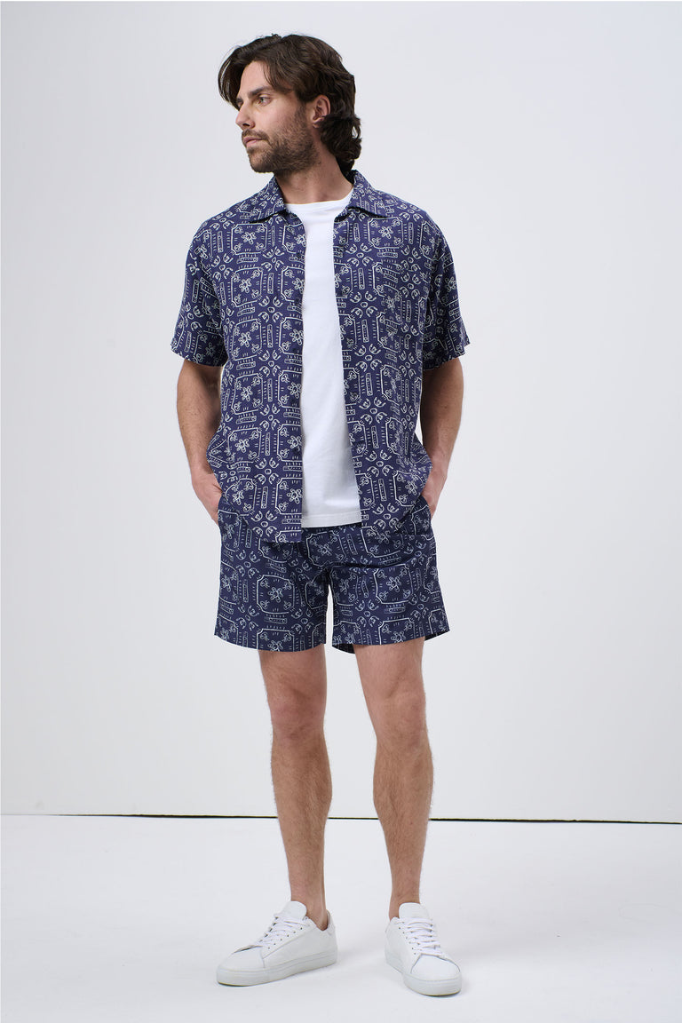 Man wearing patterned navy blue short-sleeve Cuban shirt and matching shorts with white sneakers, casual look
