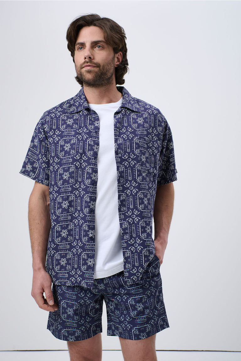 Man wearing navy patterned short-sleeve Cuban shirt paired with matching shorts and a white T-shirt underneath