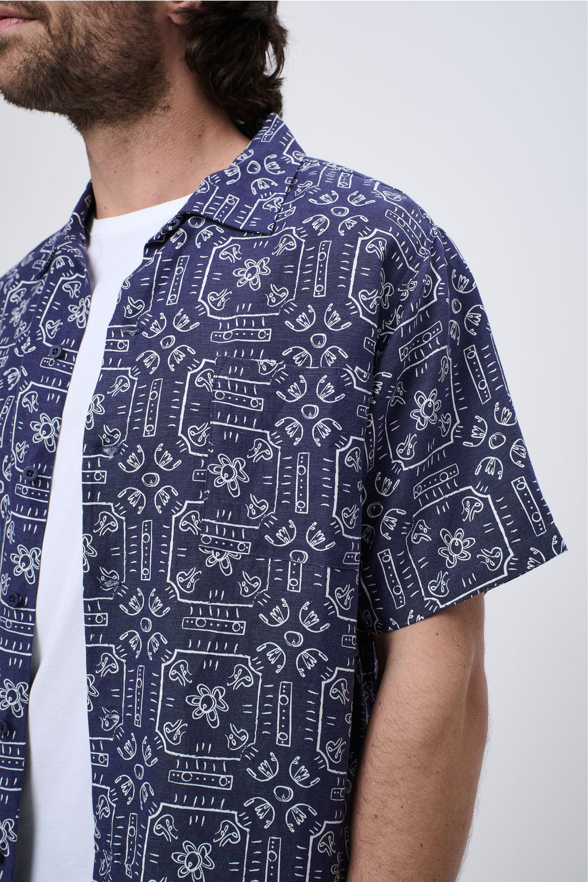 Man wearing a navy short-sleeve shirt with white geometric and floral print over a plain white tee, casual style