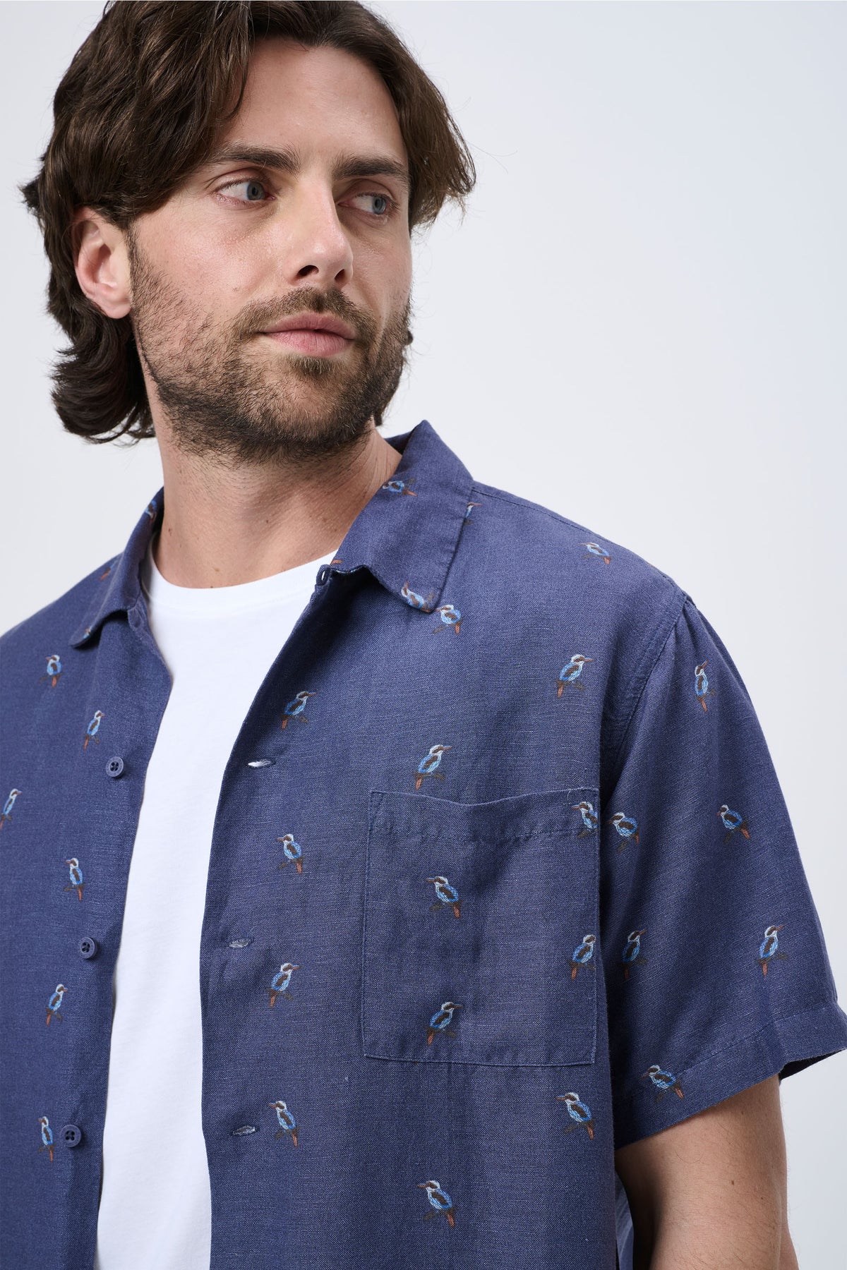 Man wearing a navy short-sleeve Cuban shirt with subtle bird embroidery over a white crew neck tee, looking sideways