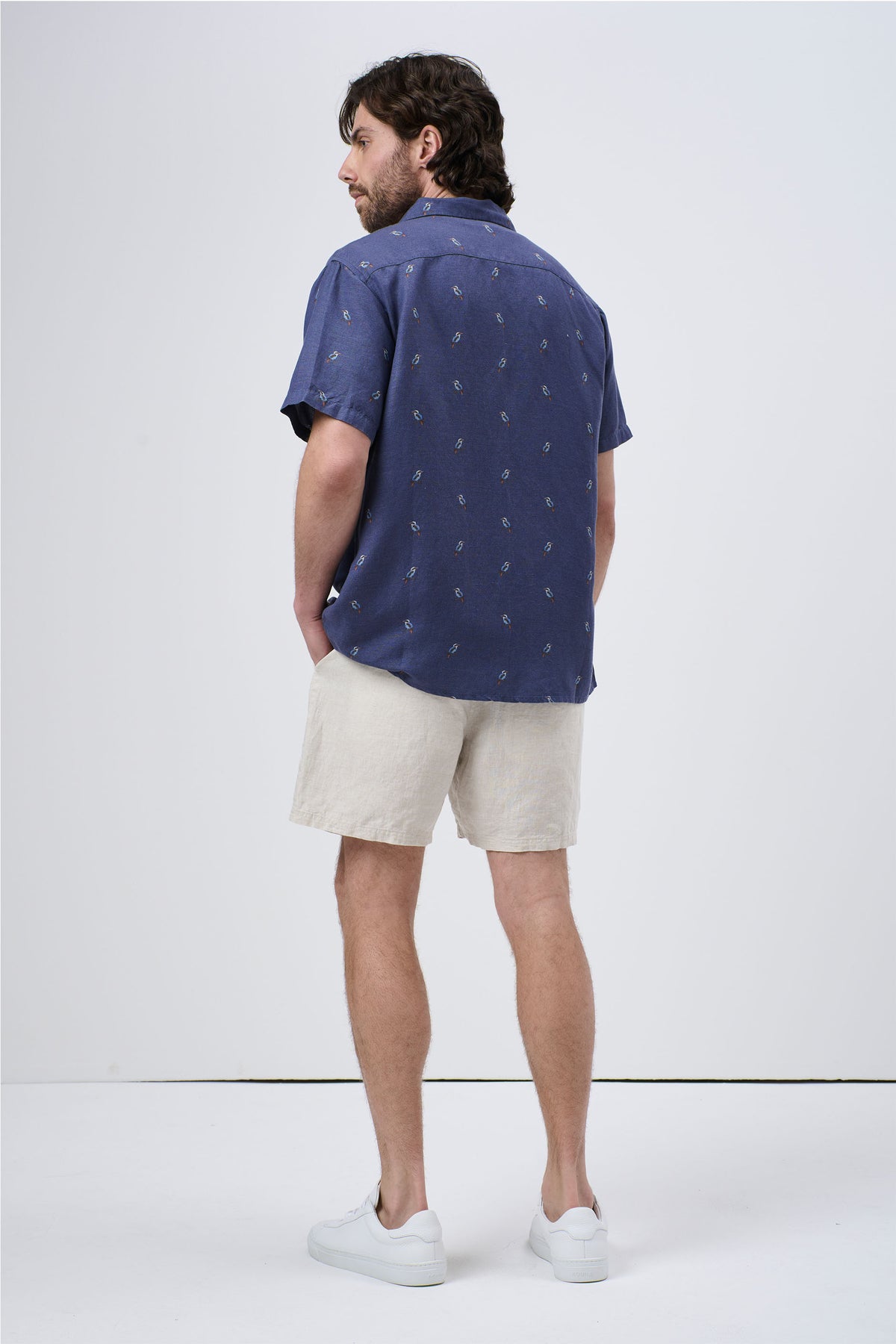Man wearing a relaxed-fit navy short-sleeve shirt with subtle print, paired with light beige shorts and white sneakers