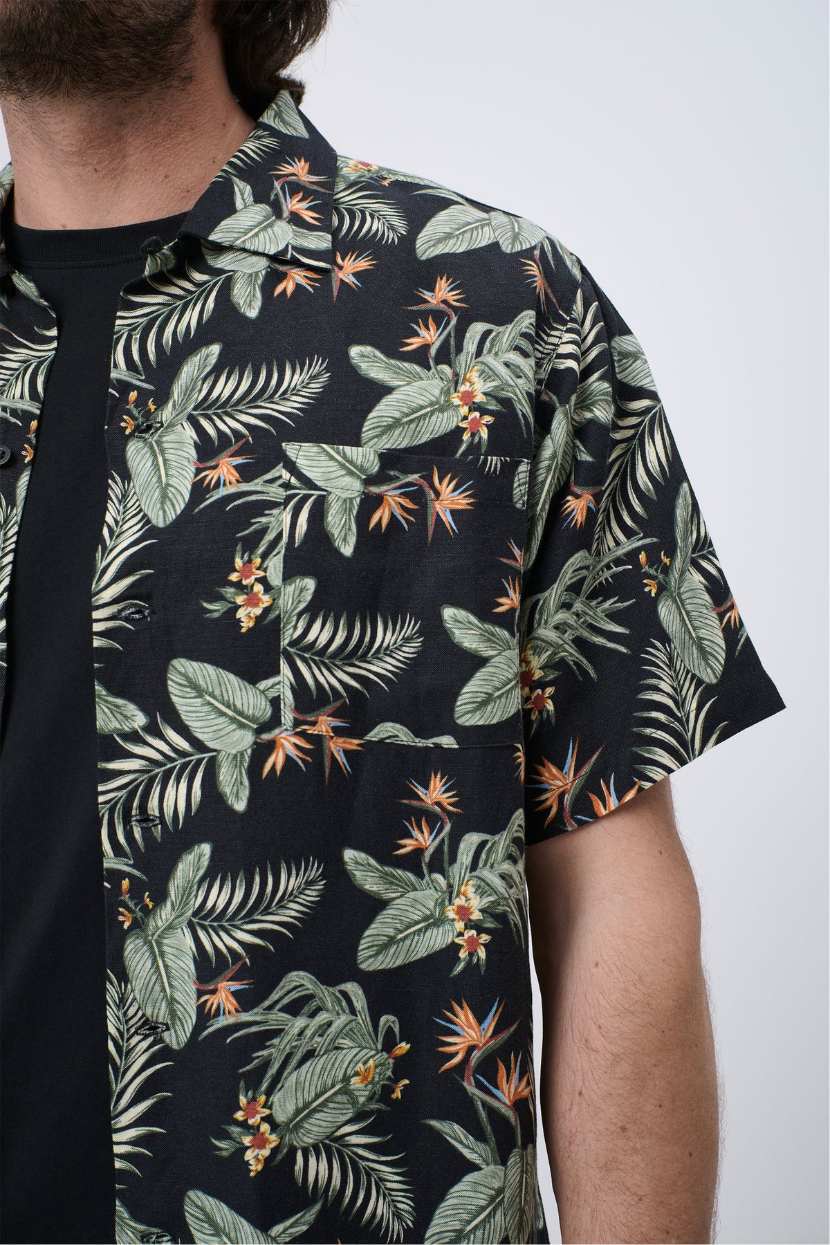 Close-up of a man wearing a black short-sleeve shirt with green tropical leaves and orange floral print, relaxed fit