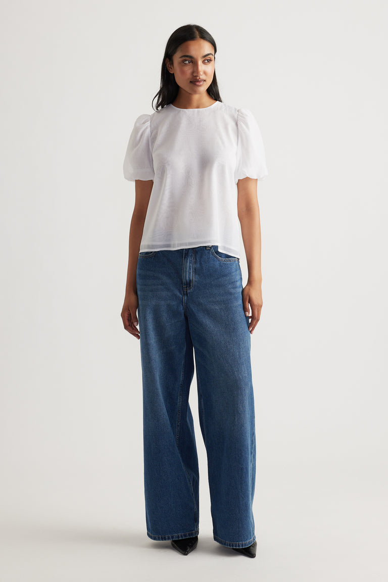 Woman wearing a white puff sleeve top paired with high-rise wide-leg blue jeans and black pointed shoes