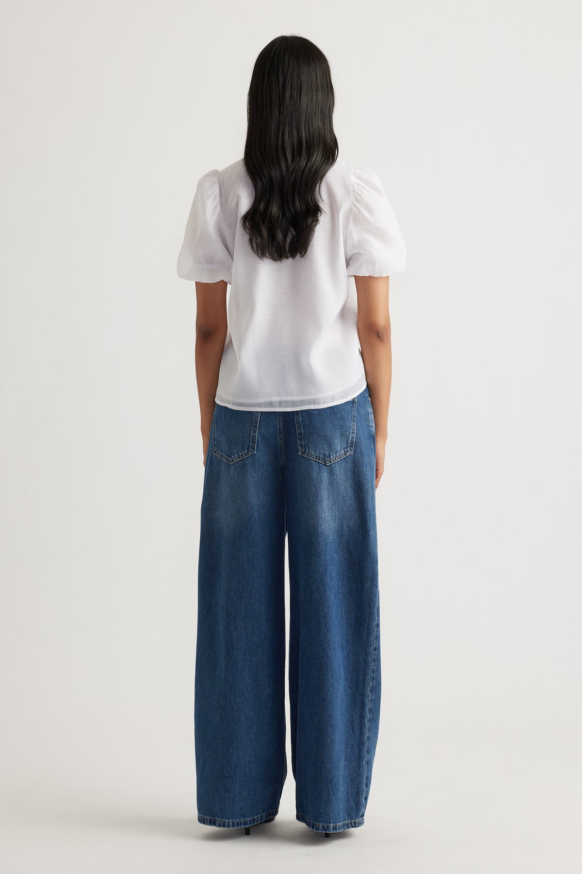 Woman seen from behind wearing white puff sleeve top paired with loose wide-leg blue denim jeans