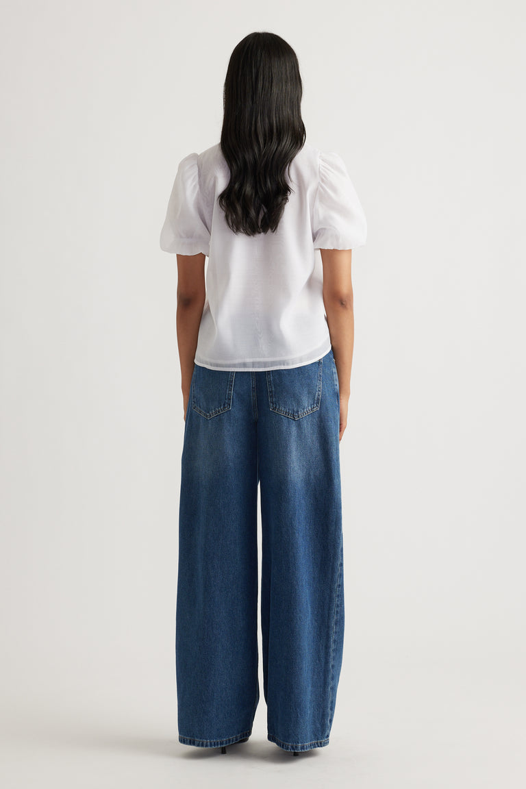 Woman seen from behind wearing white puff sleeve top paired with loose wide-leg blue denim jeans