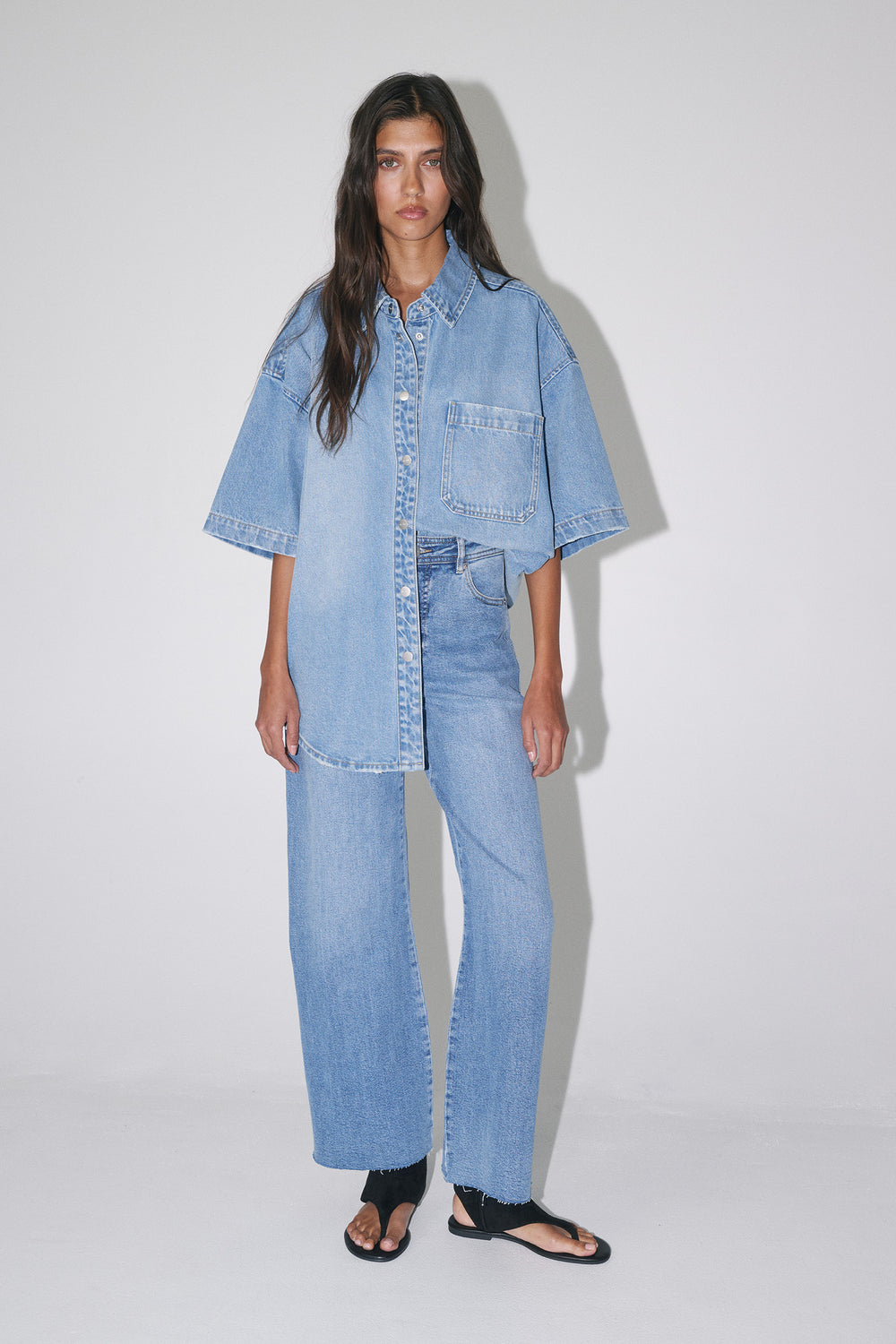 Woman wearing light wash wide-leg jeans with an oversized denim shirt and black sandals
