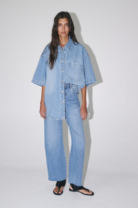 Woman wearing light wash wide-leg jeans with an oversized denim shirt and black sandals