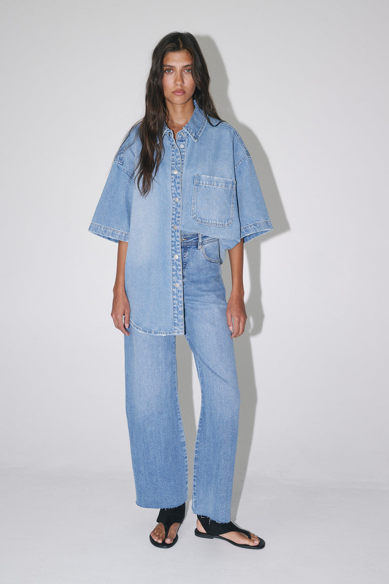 Woman wearing light wash wide-leg jeans with an oversized denim shirt and black sandals