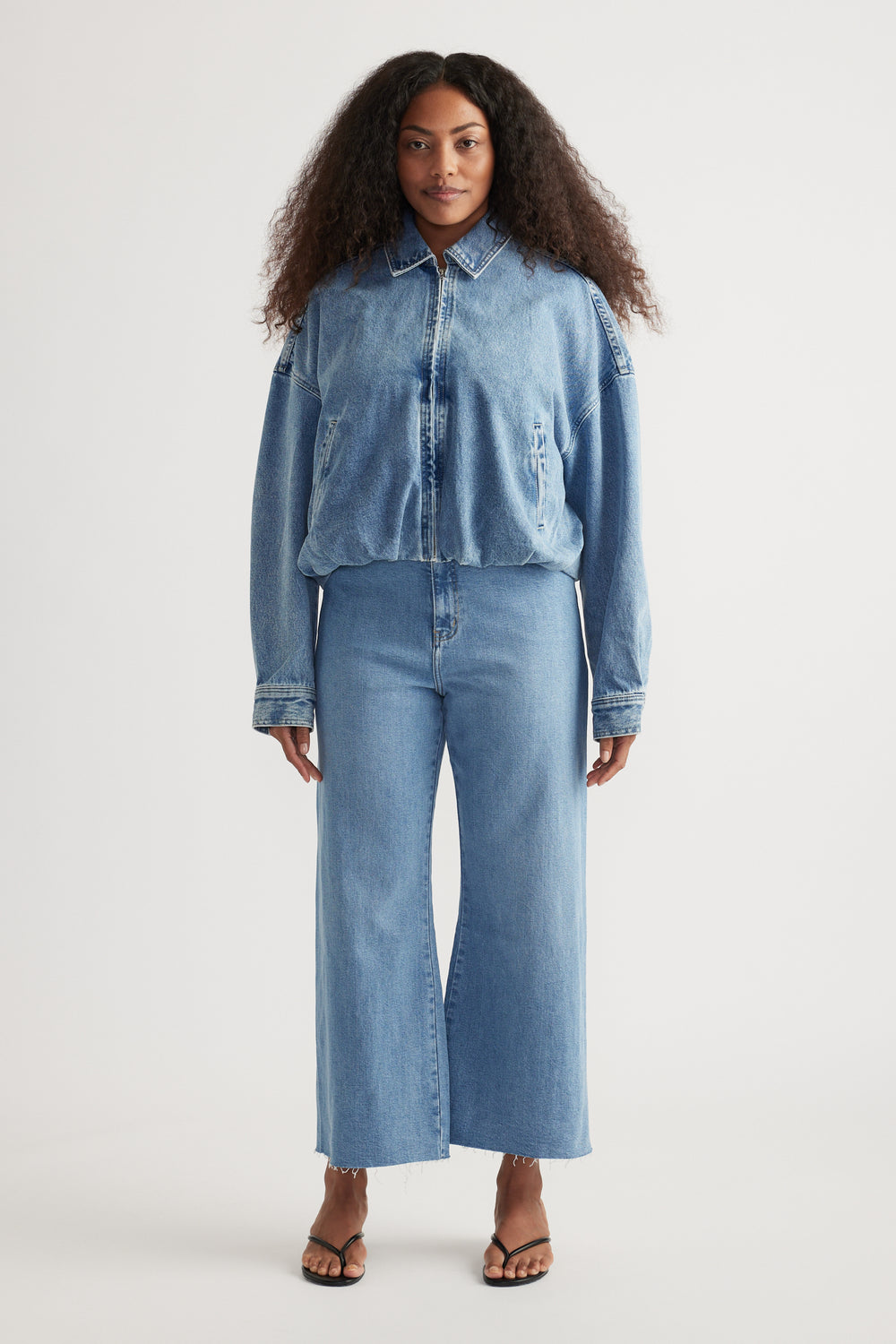 Woman wearing light blue high-rise wide-leg jeans with a cropped raw hem and strappy sandals