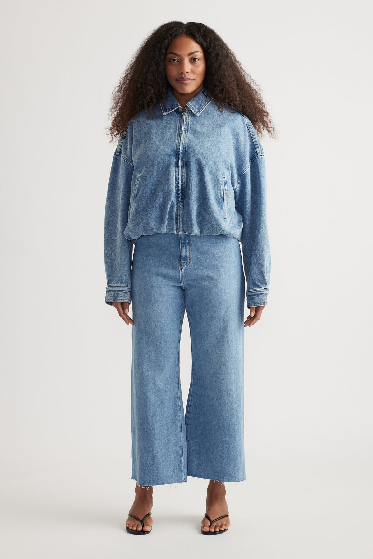 Woman wearing light blue high-rise wide-leg jeans with a cropped raw hem and strappy sandals