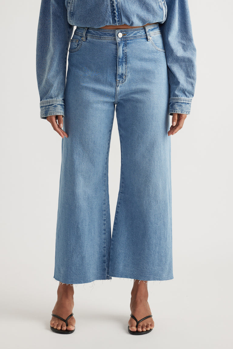 Woman wearing light blue high-rise wide-leg jeans with a cropped raw hem and black thong sandals