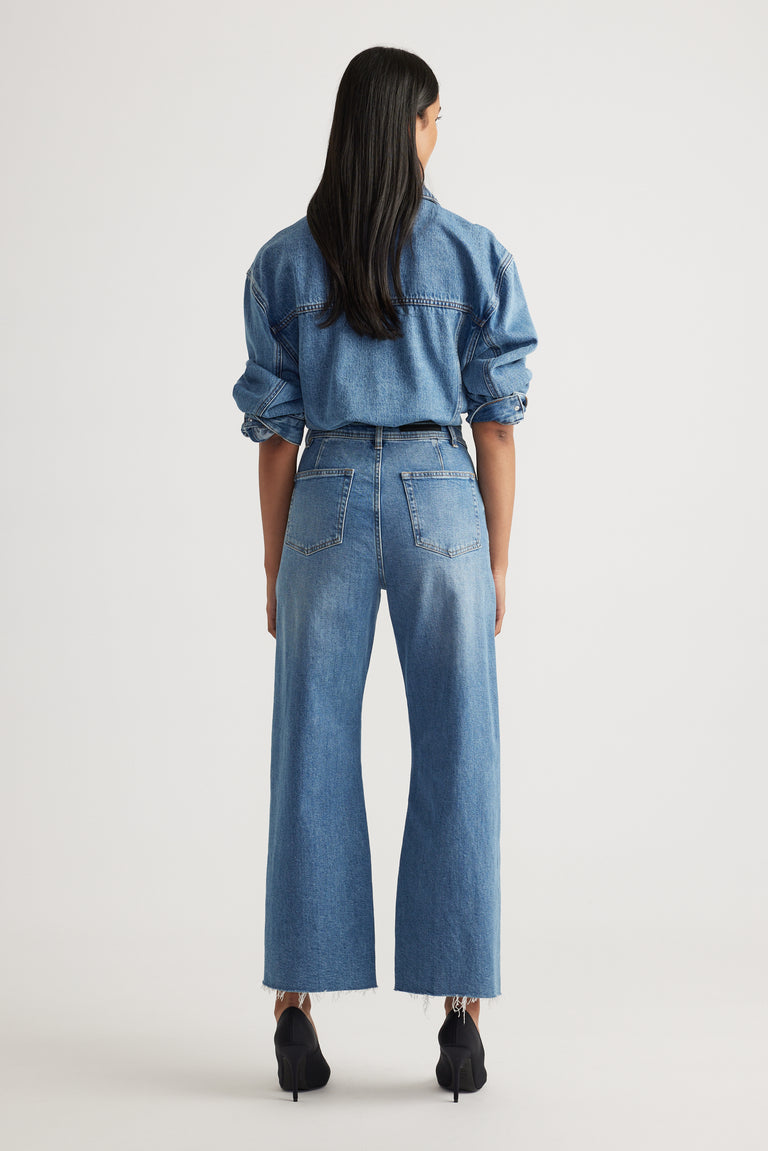 Rear view of model wearing Tahni Wide Leg Jean in light blue denim paired with oversized denim shirt by Decjuba Australian brand