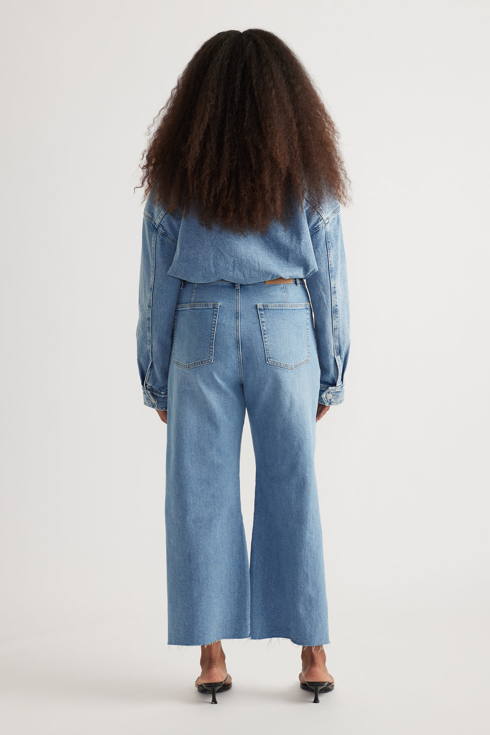 Back view of a woman wearing light blue wide-leg jeans with a cropped raw hem and back patch pockets