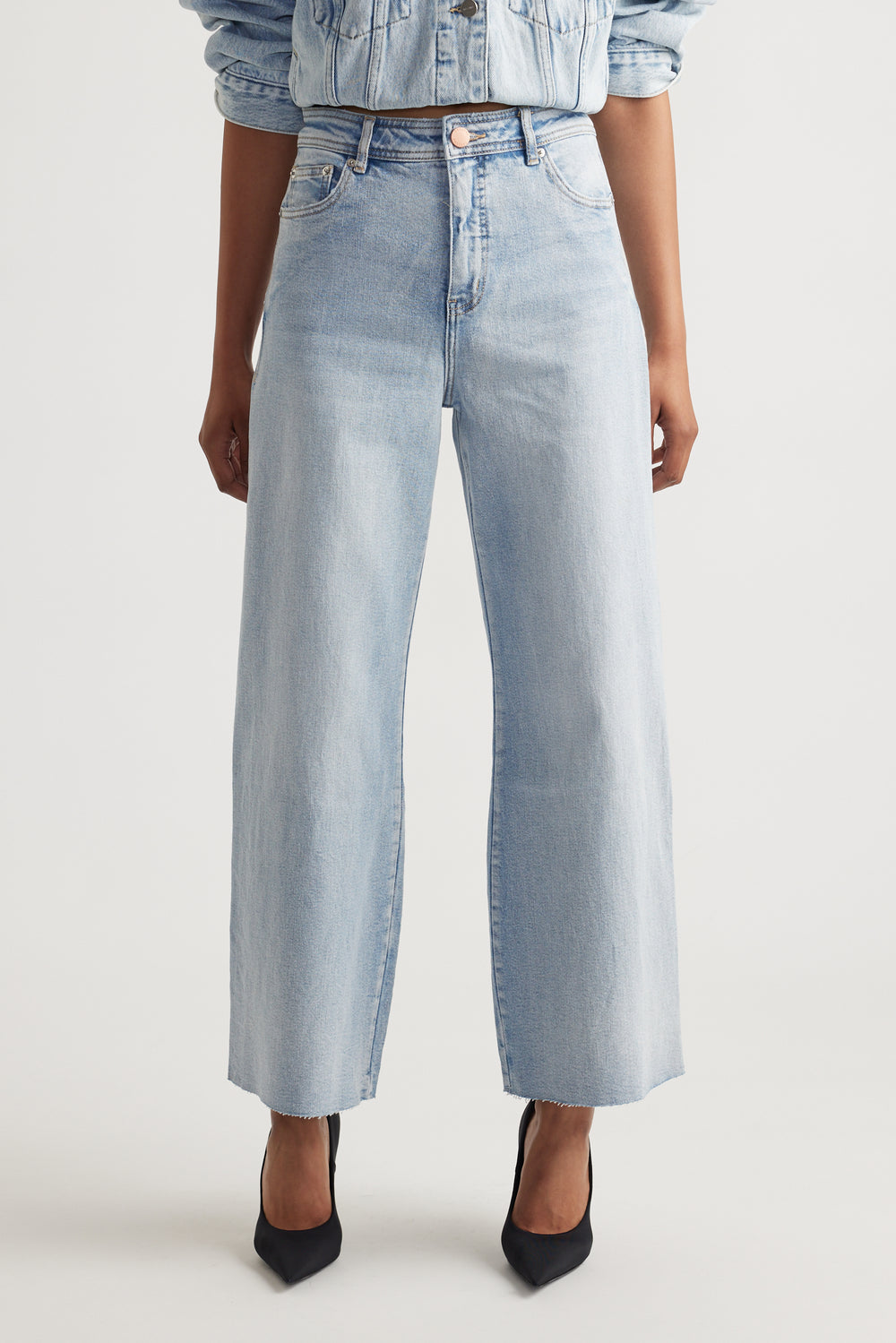 Light wash wide-leg jeans with a high waist and raw hem, styled with a matching denim jacket and black heels.