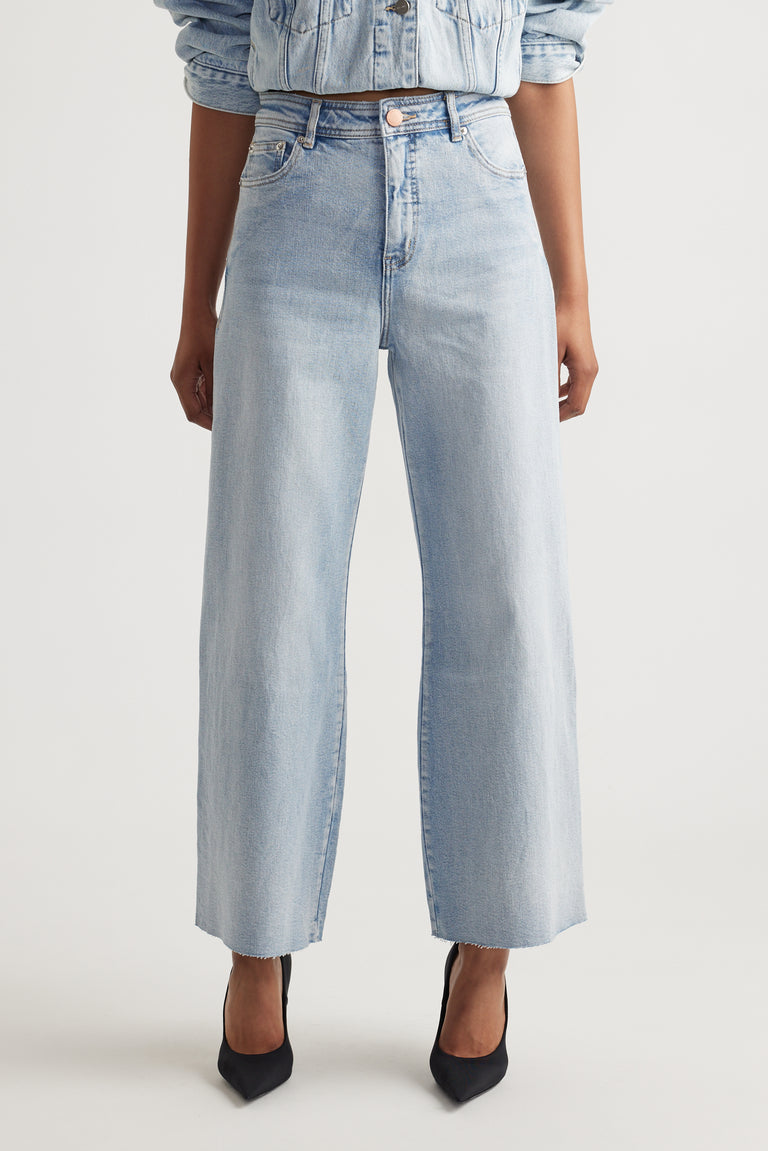 Light wash wide-leg jeans with a high waist and raw hem, styled with a matching denim jacket and black heels.