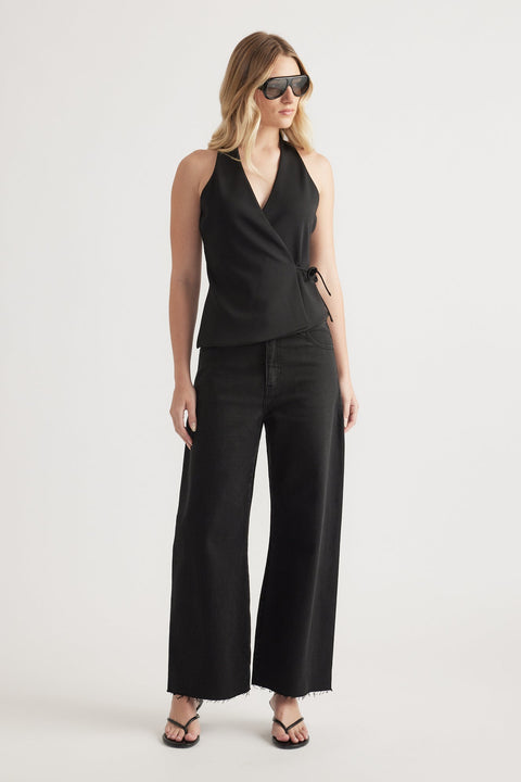 Woman wearing a sleeveless black wrap top paired with high-rise wide-leg black jeans and black sandals