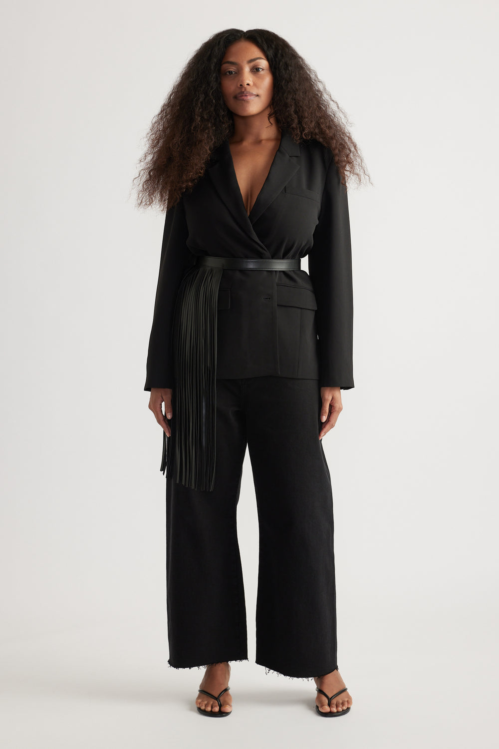 Woman wearing a black wrap top with waist belt, cropped wide leg jeans with raw hems, and strappy sandals