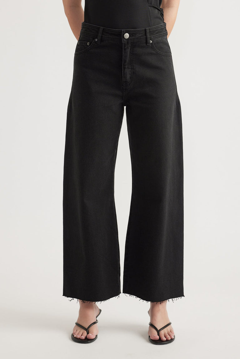 High rise black wide-leg cropped jeans with raw hem styled with black strappy sandals on a neutral background