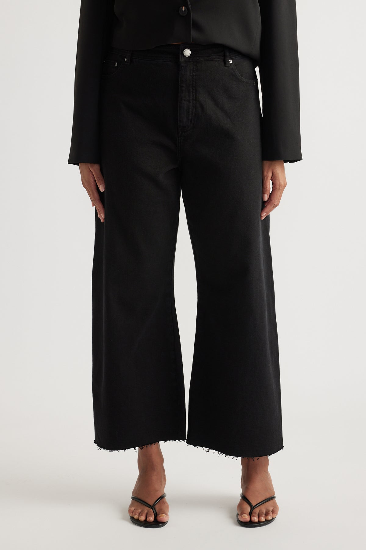 Woman wearing black high rise wide leg jeans with cropped raw hems and front pockets