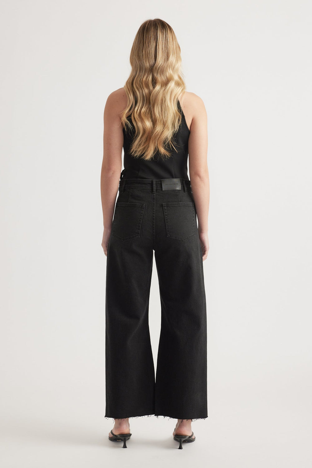 Woman wearing high-rise black wide-leg jeans with raw hem paired with a black sleeveless top and heels