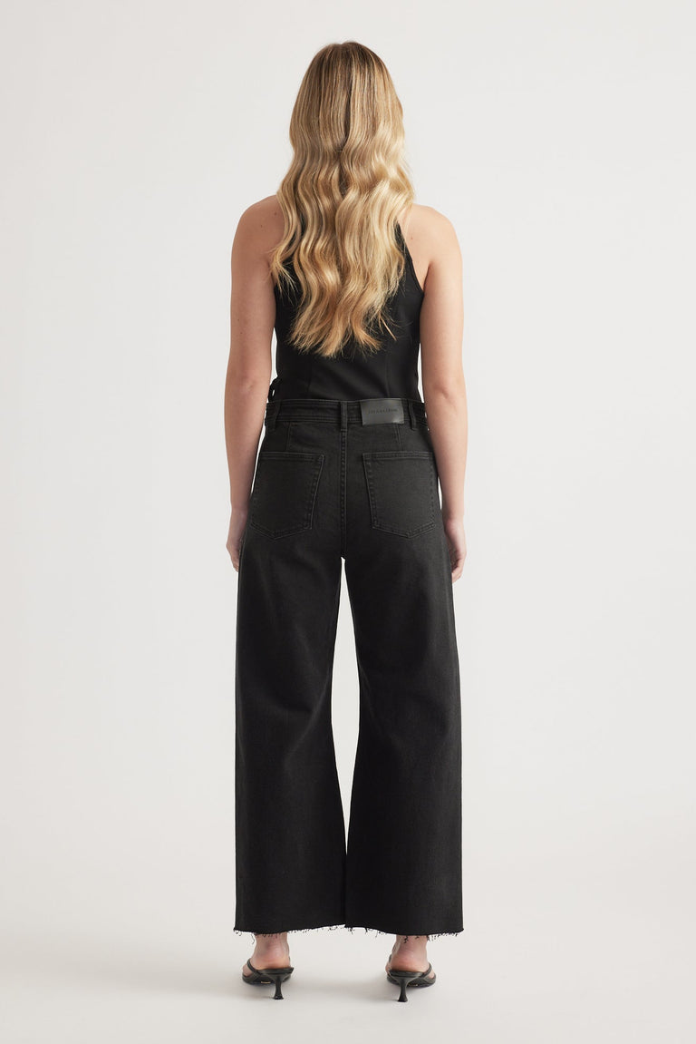 Woman wearing high-rise black wide-leg jeans with raw hem paired with a black sleeveless top and heels