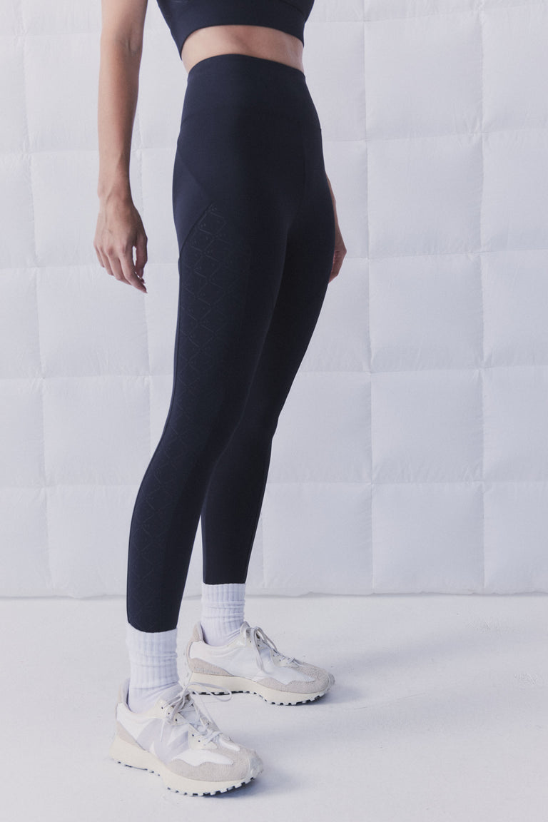 Woman wearing black high rise ankle leggings with a sculpting fit and subtle D Luxe monogram print