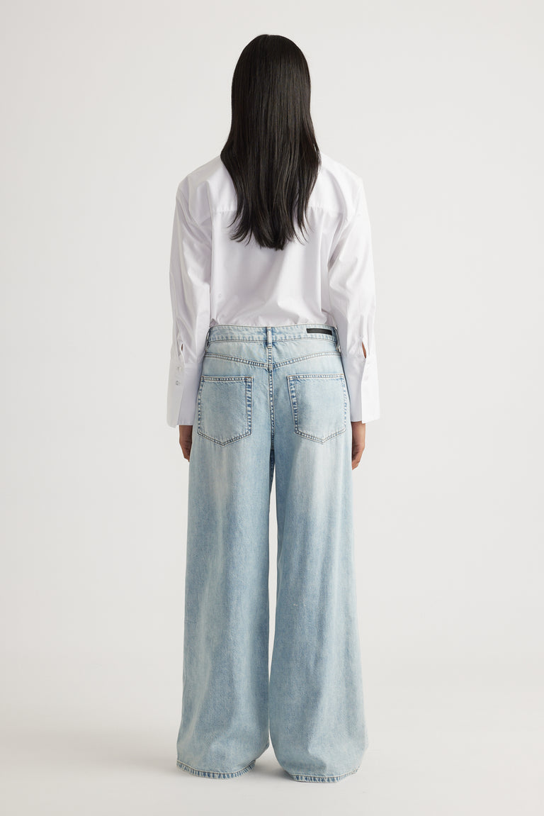 Rear view of model wearing light blue Jenna Palazzo Jean in wide leg style paired with white shirt by Decjuba Australian brand