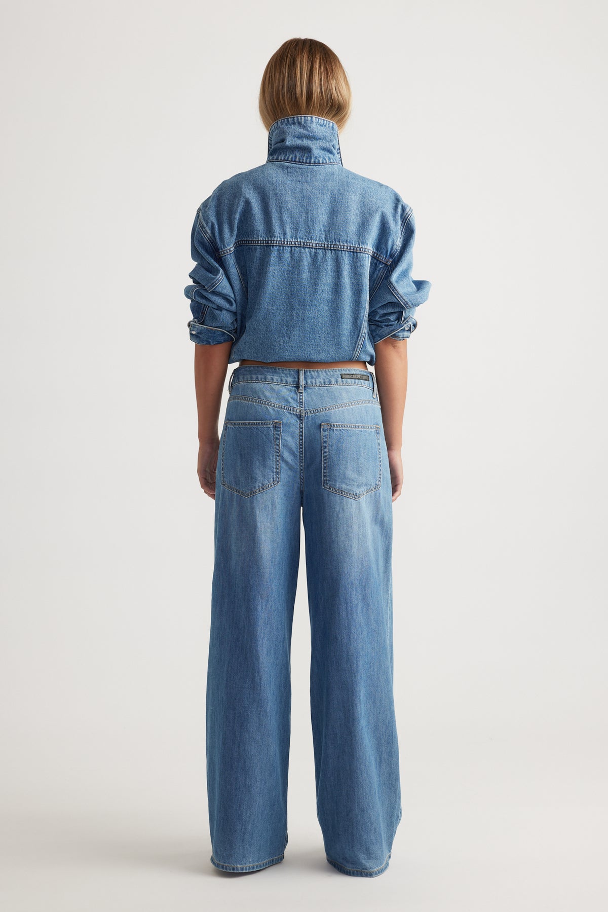 Rear view of model wearing Jenna Palazzo Jean in medium wash wide leg denim with casual denim shirt by Decjuba Australian brand