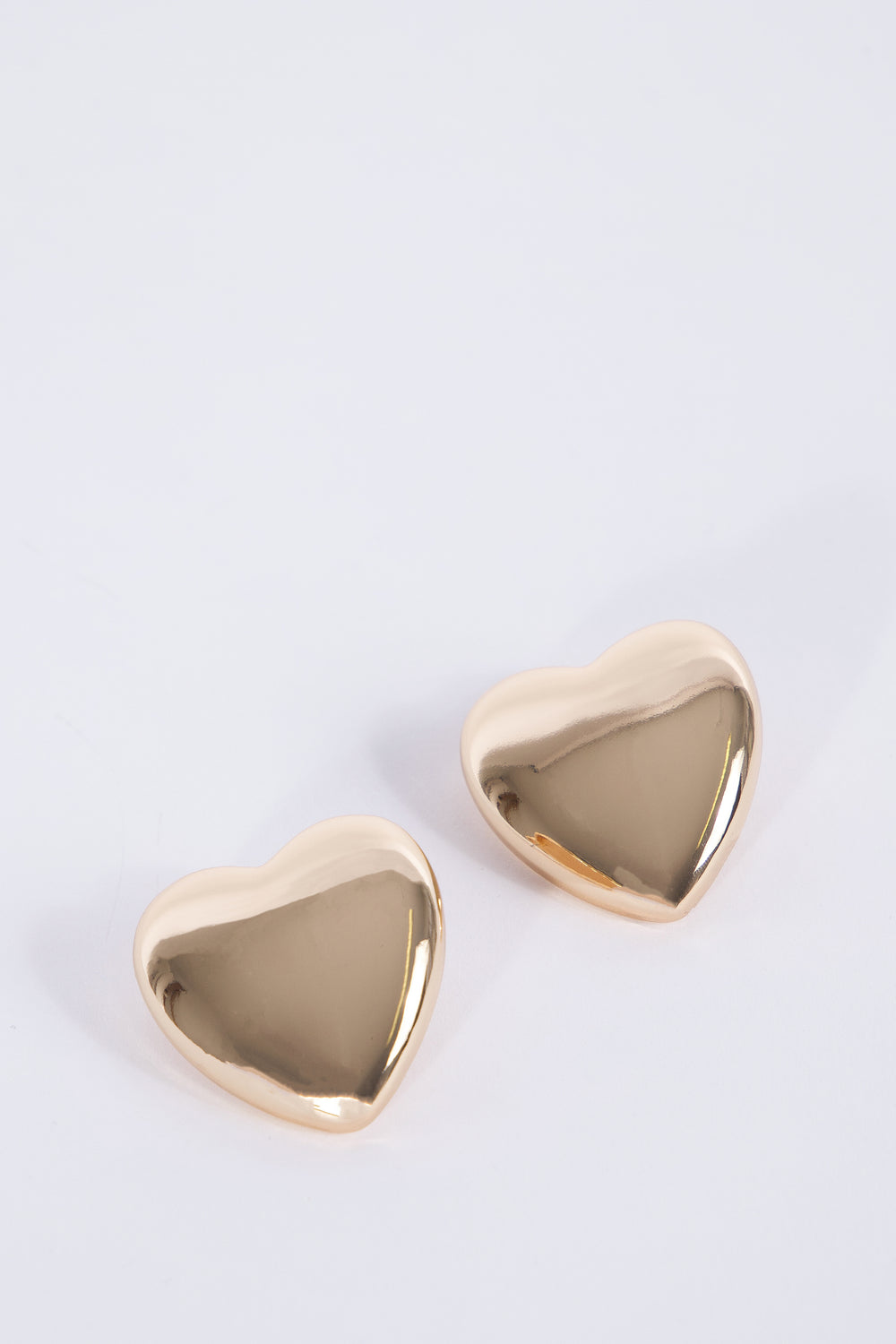 Rose gold oversized heart stud earrings on a light background