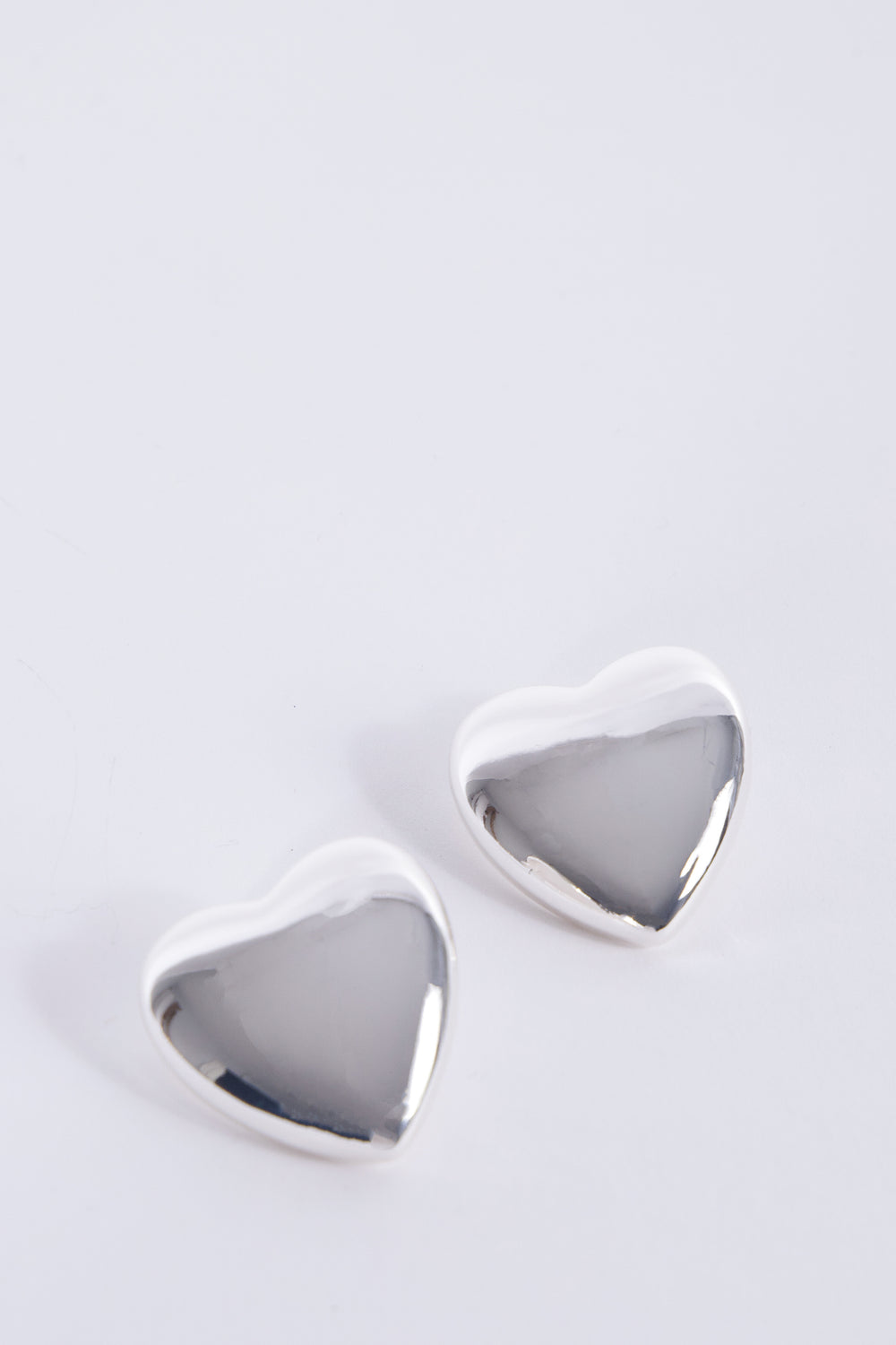 Pair of oversized silver heart stud earrings with a polished reflective finish