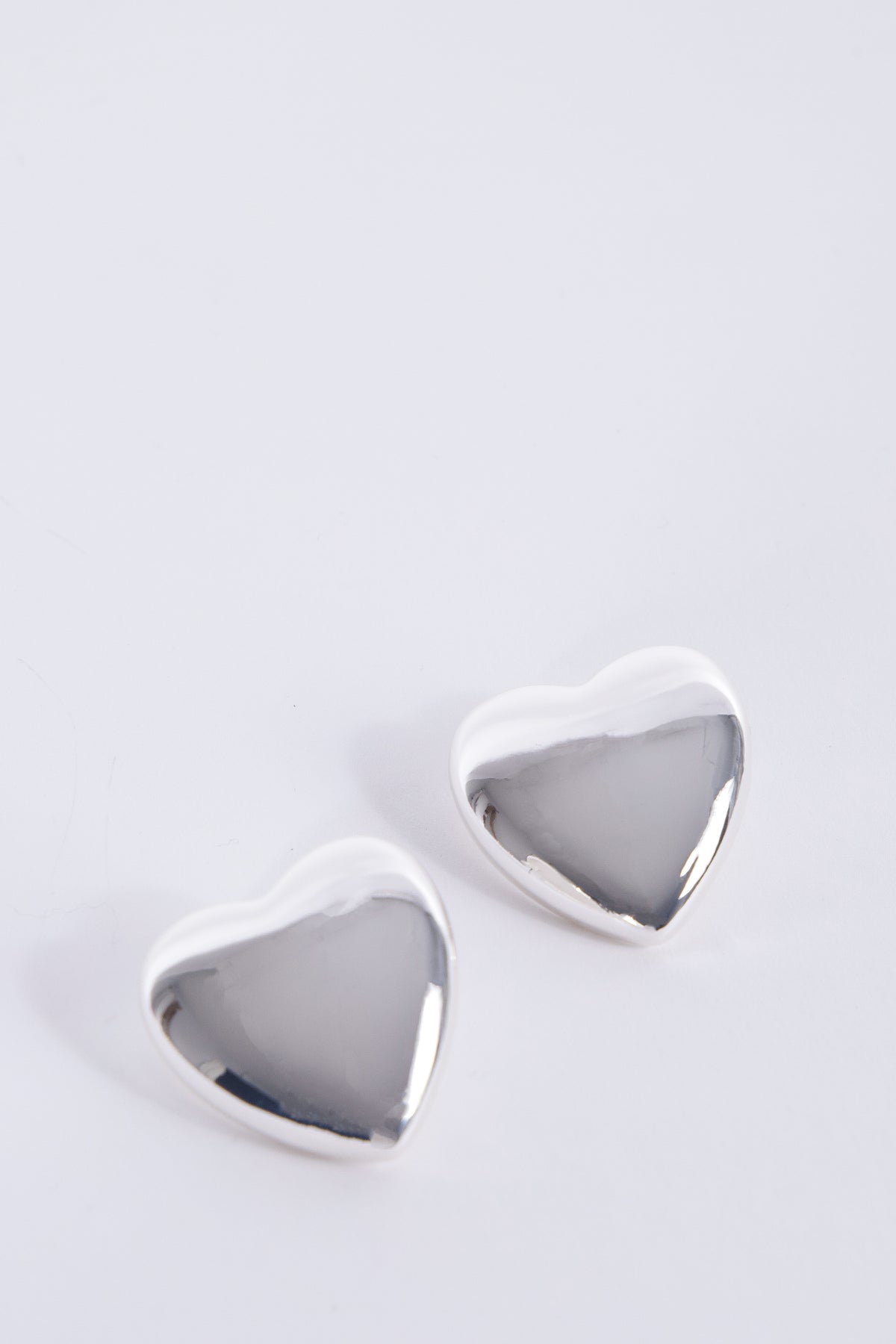 Pair of oversized silver heart stud earrings with a polished reflective finish