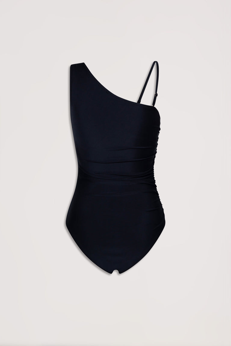 Black matte one shoulder swimsuit with ruched detailing and adjustable strap on one side against plain background