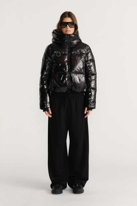 Woman wearing a shiny black puffer jacket with a high collar paired with wide-leg black pants and black sneakers.