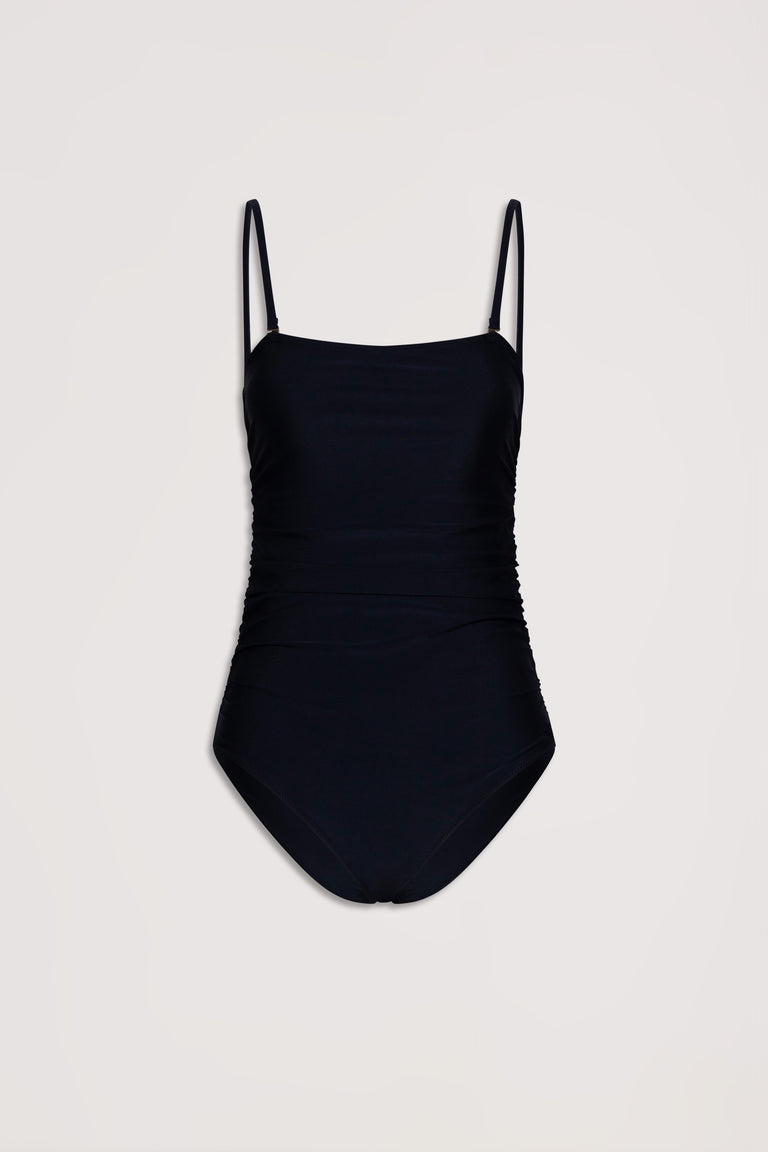 Black matte one-piece swimsuit with delicate ruched sides and thin adjustable straps on a neutral background