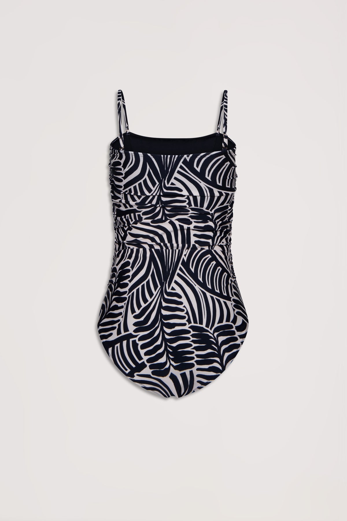 One-piece swimsuit featuring adjustable straps and a bold black and white abstract palm leaf pattern with ruched detailing