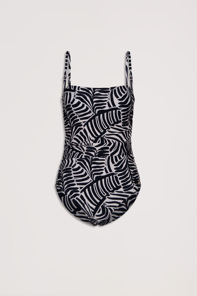 Black and beige abstract palm leaf patterned one-piece swimsuit with ruched sides and adjustable straps on a neutral background