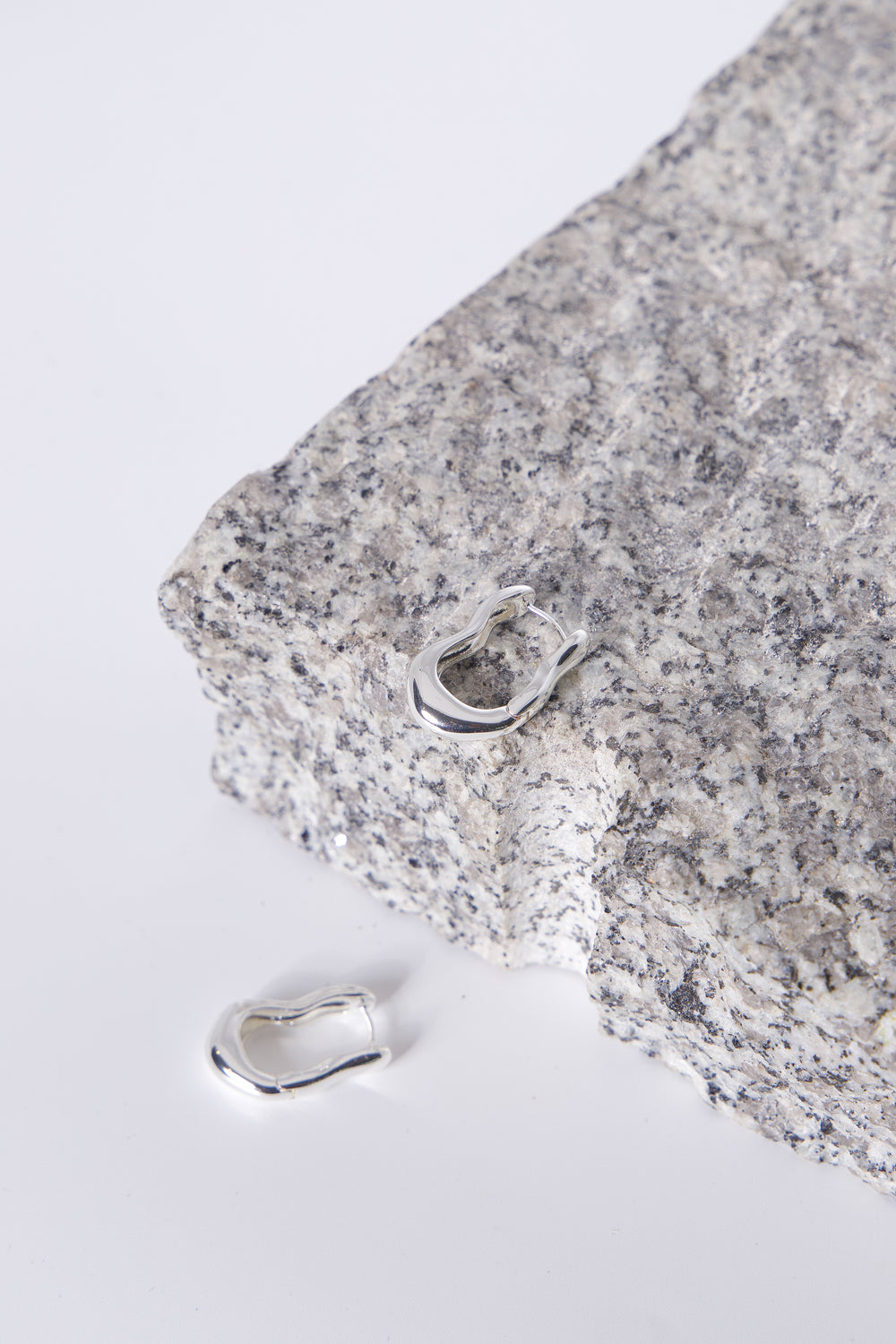 9ct Wavy Hoop Earrings in polished silver tone displayed on textured stone by Decjuba Australian fashion brand