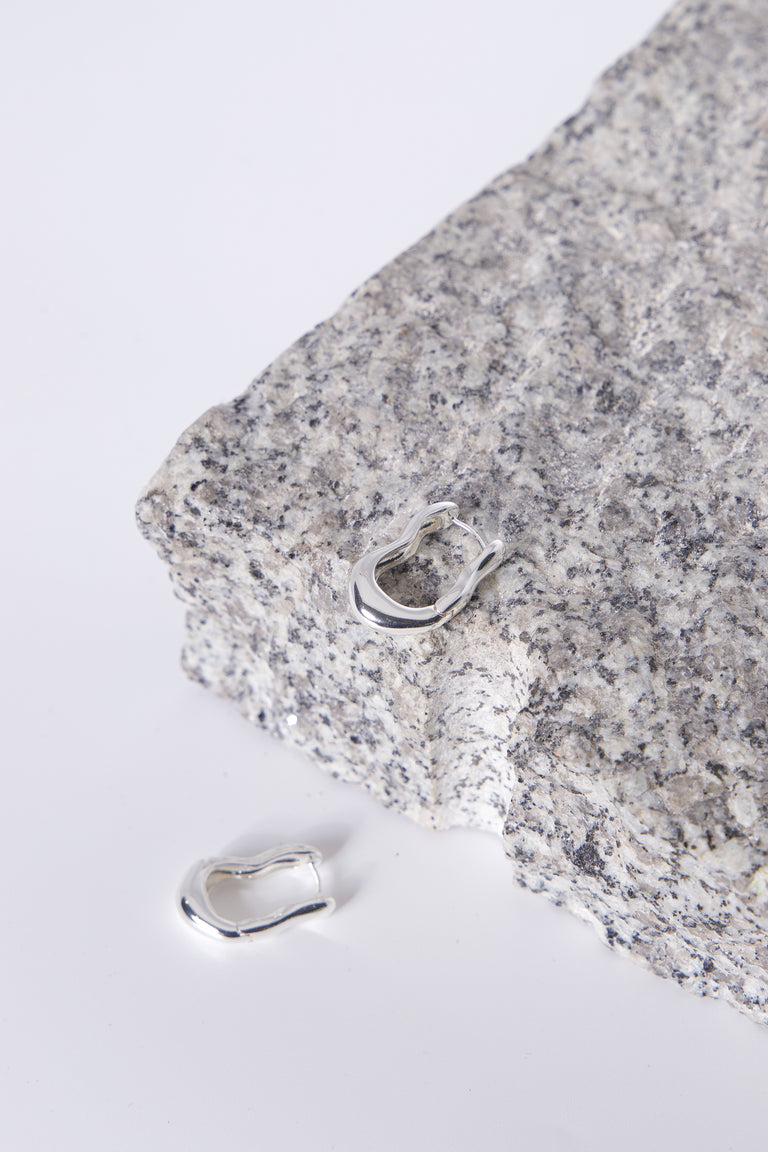 9ct Wavy Hoop Earrings in polished silver tone displayed on textured stone by Decjuba Australian fashion brand