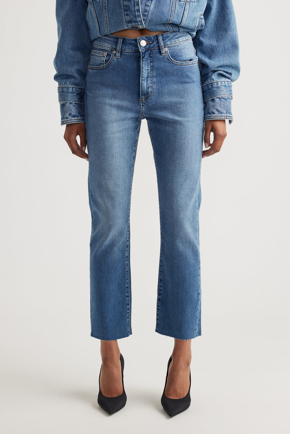 Front view of mid-rise straight-leg blue denim jeans styled with a cropped denim jacket and black pointed heels