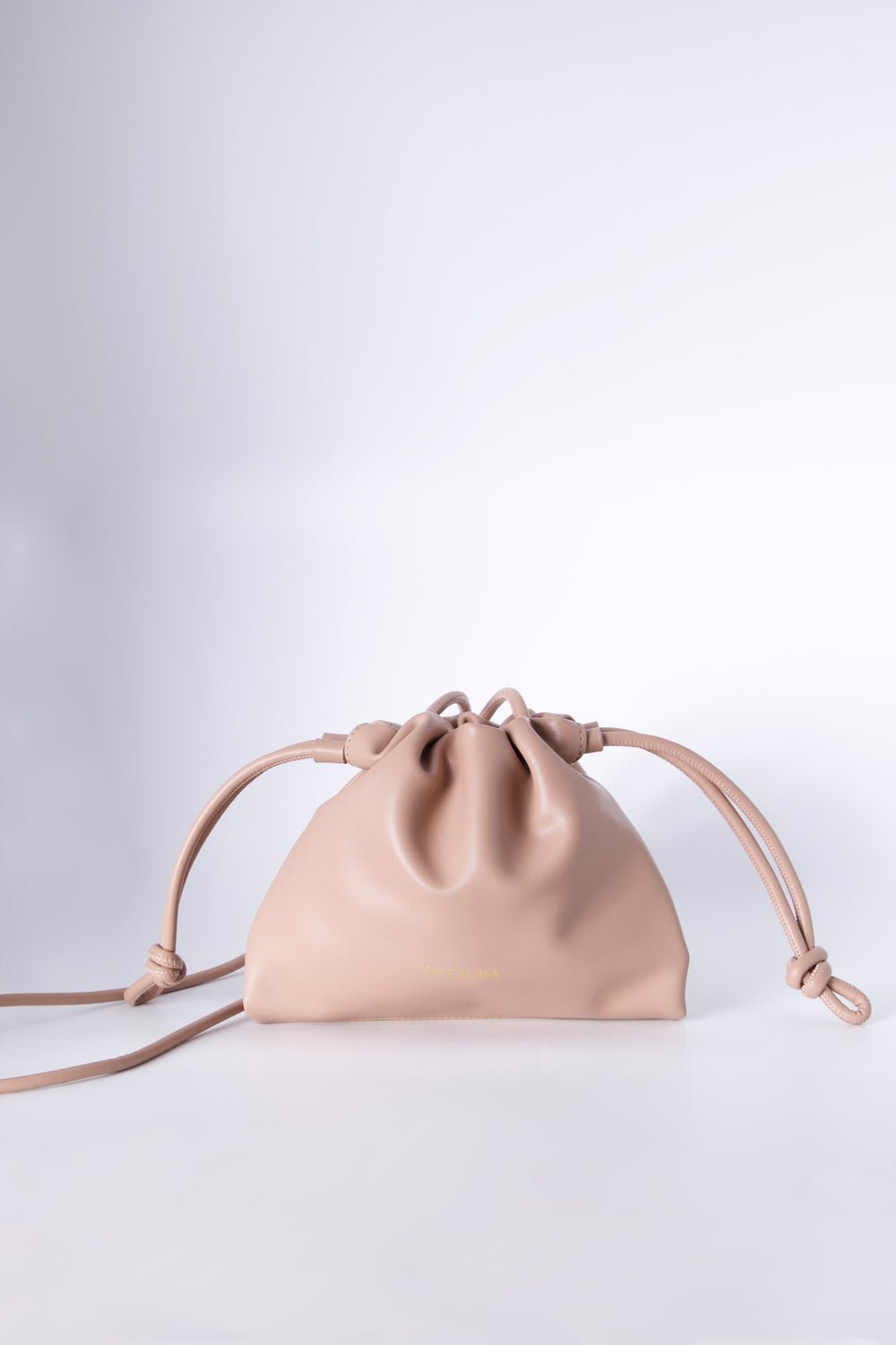 Blush drawstring sling bag with a thin strap and gathered closure