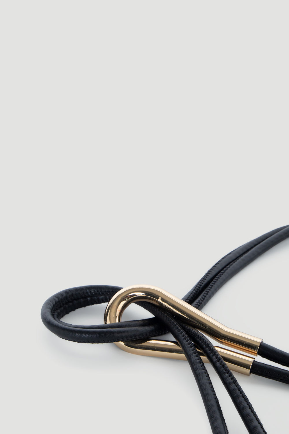 Close-up of a sleek black thin belt looped through a polished gold metal clasp for a minimalist look.