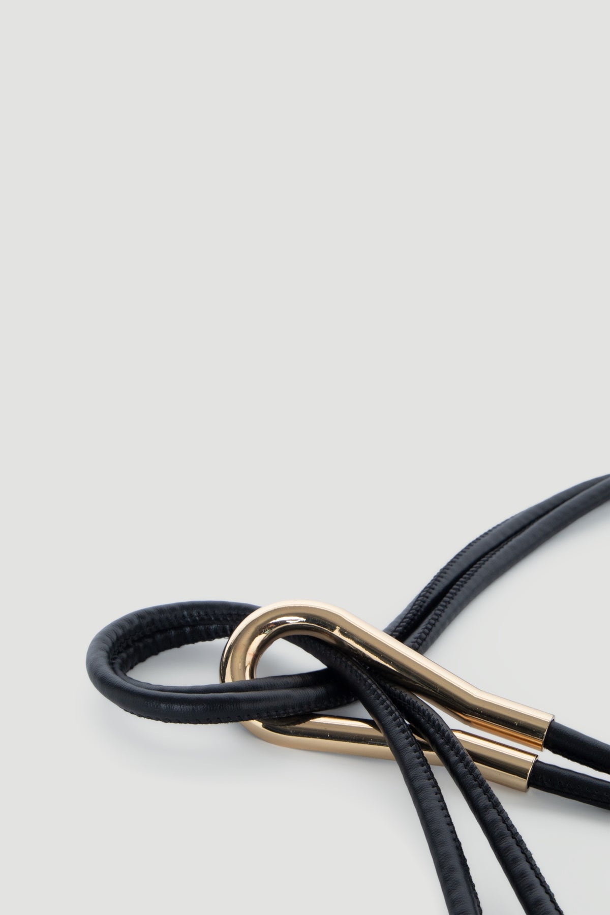 Close-up of a sleek black thin belt looped through a polished gold metal clasp for a minimalist look.