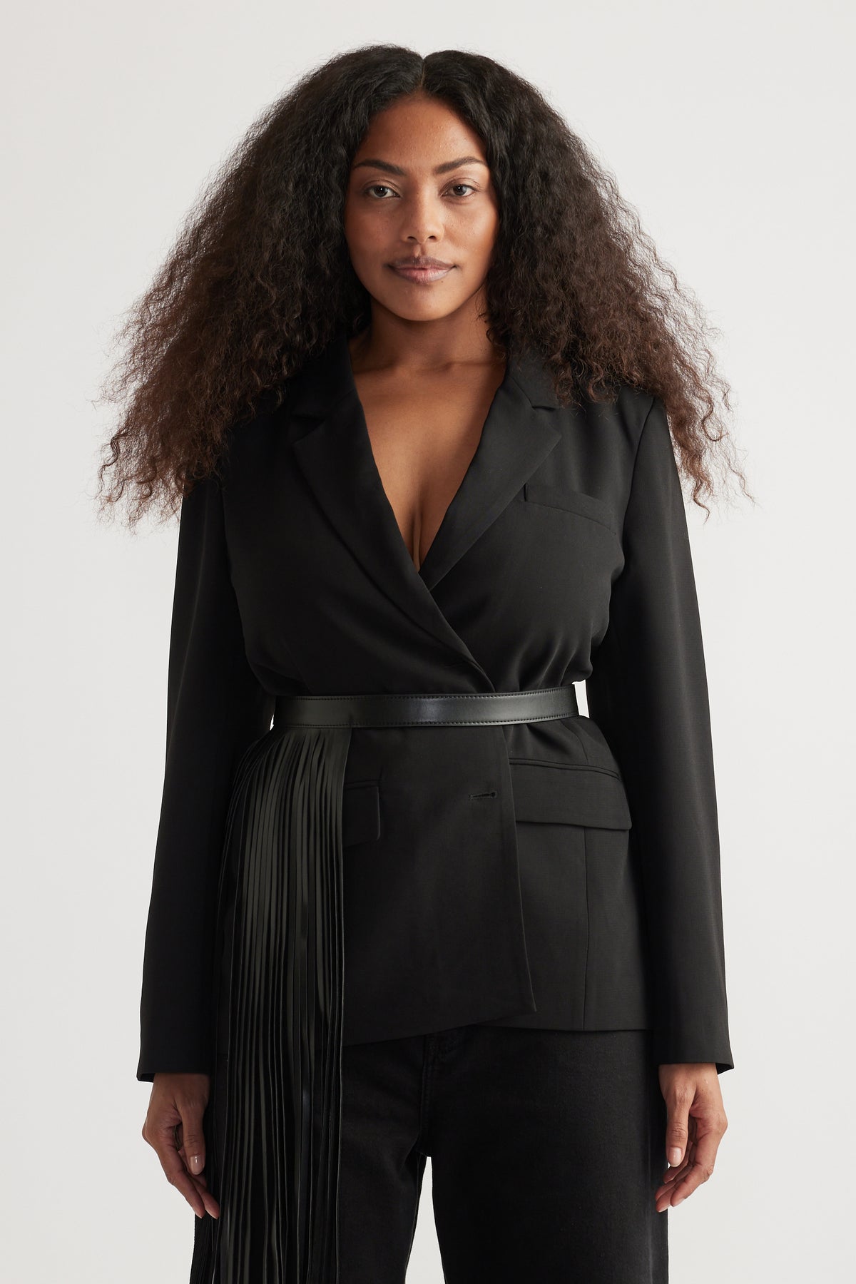 Woman wearing a black oversized tailored blazer with peak lapels, belted waist and front pockets
