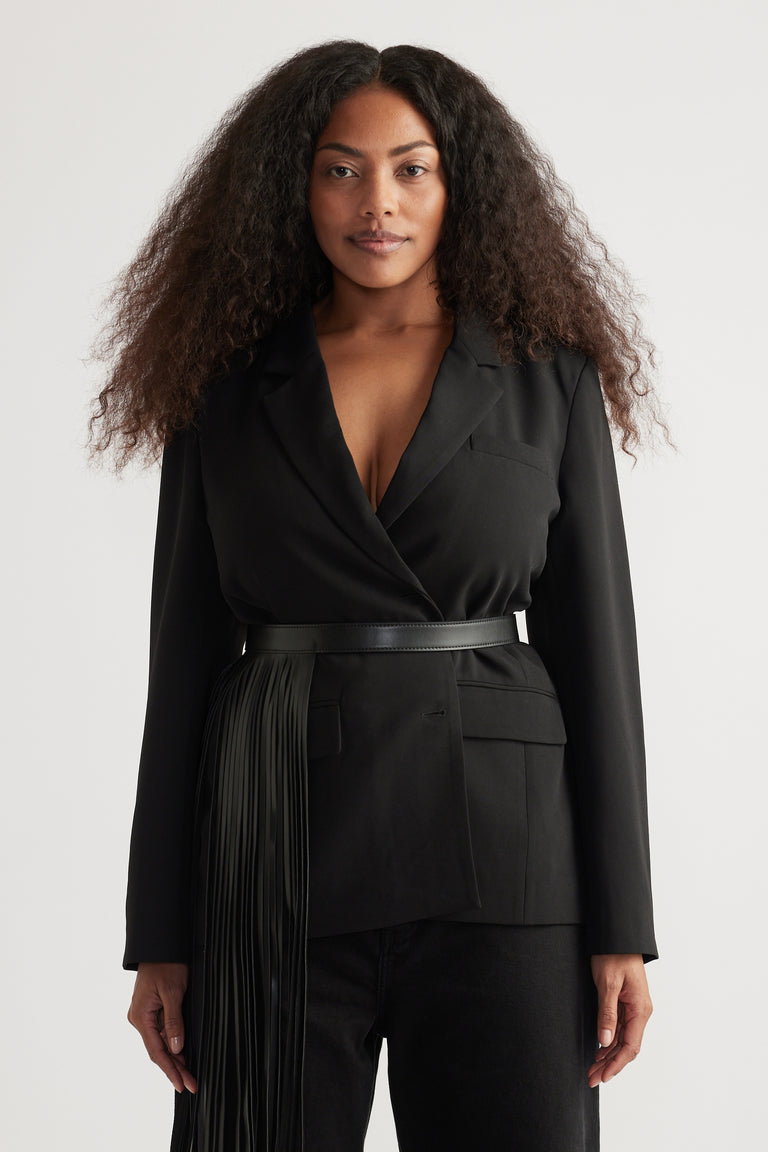 Woman wearing a black oversized tailored blazer with peak lapels, belted waist and front pockets