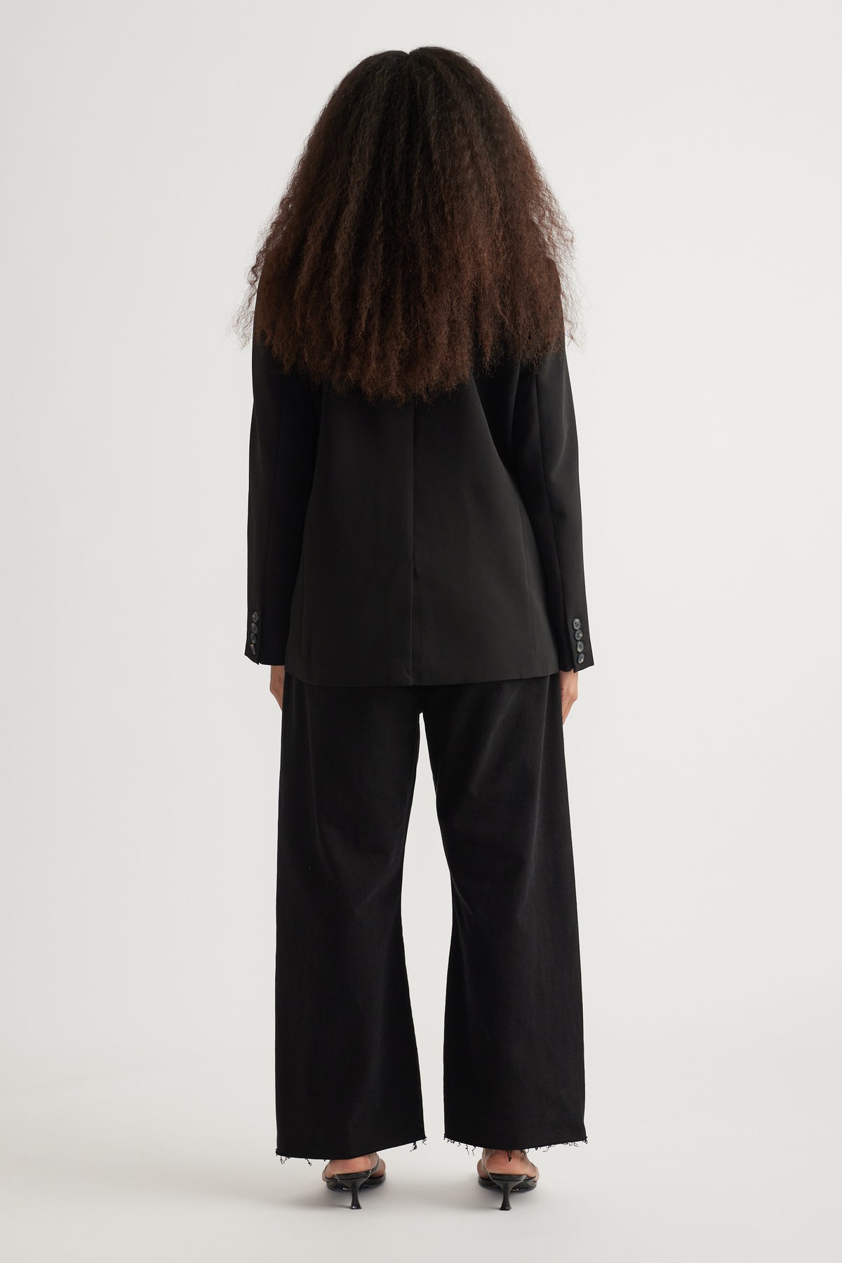 Back view of woman wearing an oversized black tailored blazer with wide-leg black pants and heels
