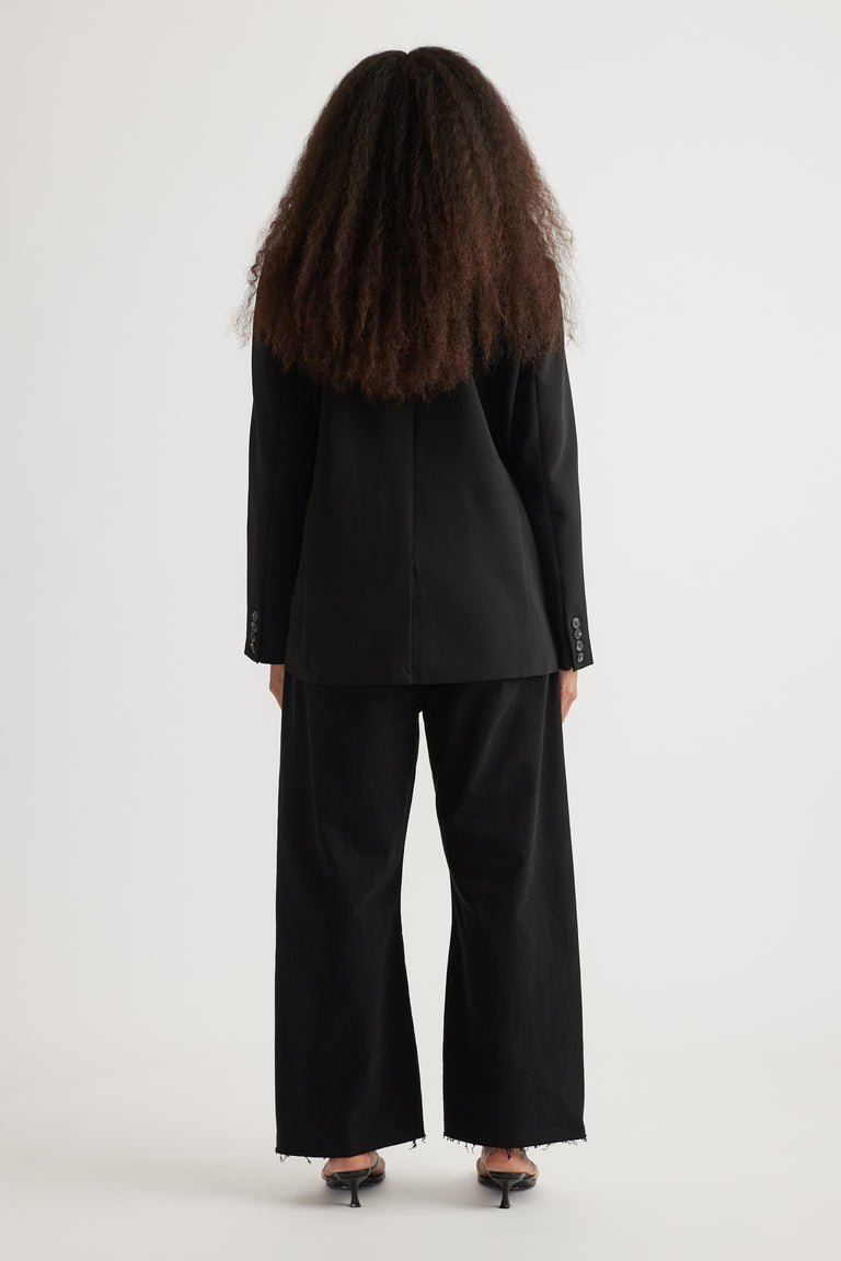Back view of woman wearing an oversized black tailored blazer with wide-leg black pants and heels